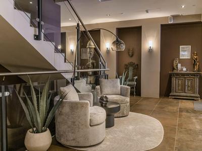 Modern hotel lobby with armchairs, rug, and plants under a staircase.