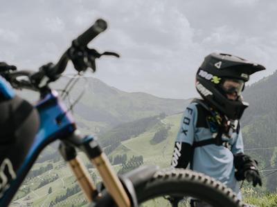 Fahrradfahrer mit Helm auf Berg mit grünem Tal und bewölktem Himmel.