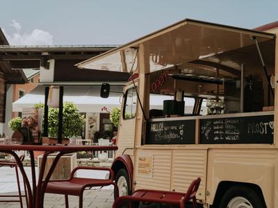 Gemütlicher Außenbereich eines Cafés mit einem verkaufswagenartigen Getränkestand und roten Tischen.