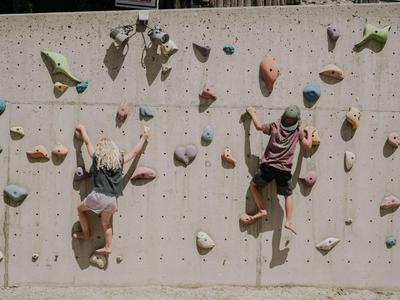 Zwei Personen klettern an einer hellen Kletterwand mit bunten Griffen.