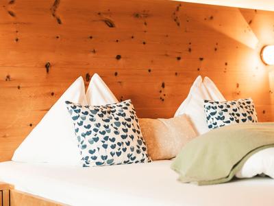 Gemütliches Doppelbett mit Kissen und Holzwand im Hintergrund, warme Beleuchtung.