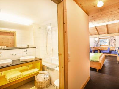 Helles Hotelzimmer mit Holzwänden, Bett, Sitzecke und Badezimmer mit Doppelwaschbecken.