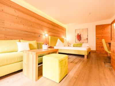 Helles Hotelzimmer mit Holzmöbeln, Doppelbett und gelbem Sofa.