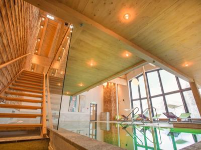 Helles Hallenbad mit Holzdecke, Glastüren und Treppe in einem modernen Hotel.