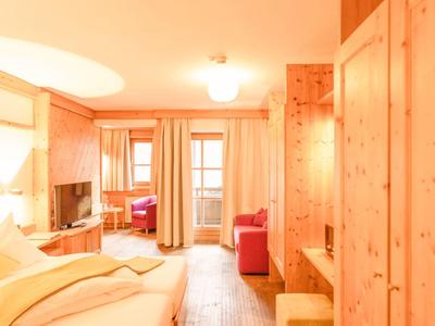 Helles Hotelzimmer mit Holzfußboden, Bett, Schrank und Zugang zum Balkon mit Vorhängen.