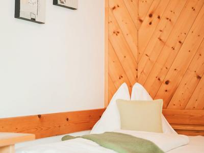Gemütliches Einzelbett in einem Holzzimmer mit grüner Decke und Kissen.