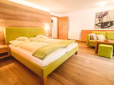 Helles Hotelzimmer mit grünem Doppelbett, Holzboden und einer grünen Couch mit Hockern.