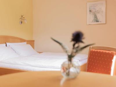 Ein helles Hotelzimmer mit einem weißen Bett, einem roten Stuhl und einer Vase mit einer Blume auf dem Tisch.