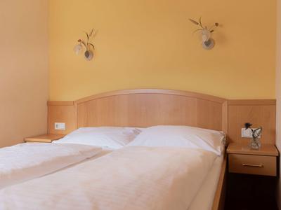 Schlicht eingerichtetes Hotelzimmer mit Doppelbett, Nachttisch und gelben Wänden.