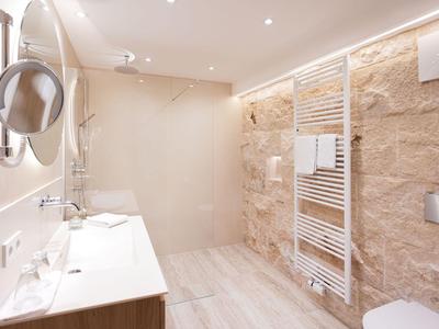 Modernes Bad mit Waschbecken, Glasdusche und Natursteinwand in hellem Design.