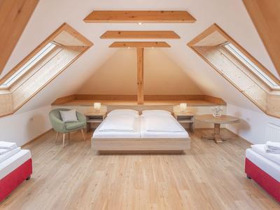 Modernes Hotelzimmer unter Dachschrägen mit Doppelbett und zwei Einzelbetten.