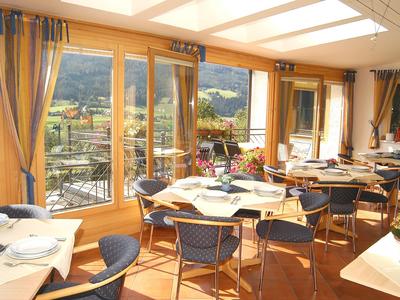 Helles Restaurant mit großen Fenstern und Tischen mit weißen Tischdecken, Blick auf Berglandschaft.