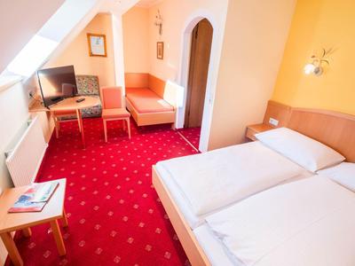 Helles Hotelzimmer mit Doppelbett, rotem Teppich und Sitzbereich mit Fernseher.