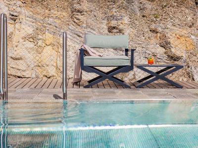 Pool mit klarem Wasser, Holzdeck, schwarzem Stuhl und Tisch vor Felsenwand.
