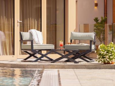 Zwei gepolsterte Stühle und ein kleiner Tisch auf einer Terrasse neben einem Pool.