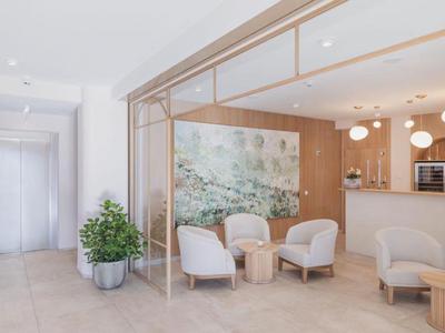 Moderner Hotel-Loungebereich mit Sesseln, rundem Holztisch und großer Pflanzen in hellen Tönen.