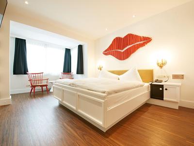 Habitación de hotel moderna con cama grande, suelo de madera y decoración mural de labios rojos.