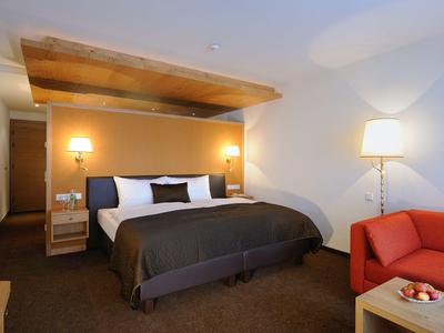 Habitación de hotel moderna con cama grande, acentos cálidos de madera y zona de estar acogedora.
