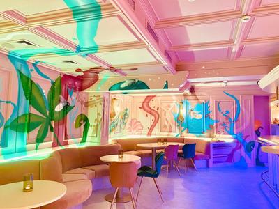 Área de bar moderna en hotel con murales coloridos, mesas redondas y asientos variados.