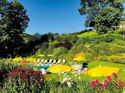 Área de piscina con sombrillas amarillas, tumbonas y entorno verde bajo cielo despejado.