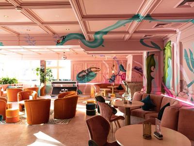 Elegante salón de hotel con paredes rosas, murales coloridos y asientos cómodos.