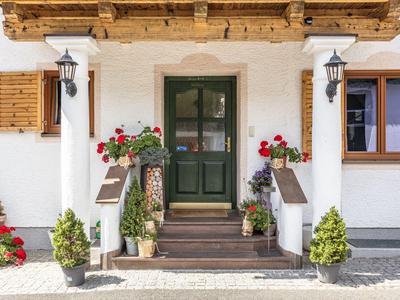 Eingang eines Hotels mit grüner Tür, Pflanzen und Blumenkästen unter dem Holzdach.