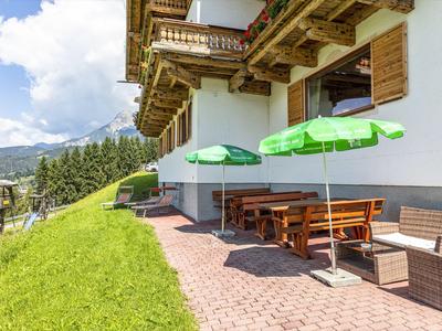 Außenbereich eines Hotels mit Holzbänken, grünen Sonnenschirmen und Blick auf Berge.