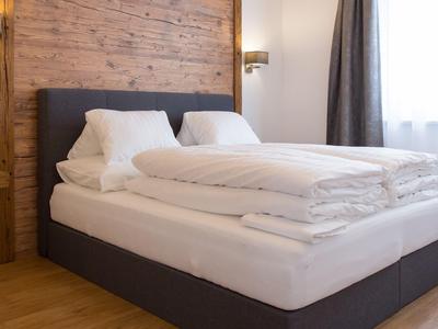 Modernes Hotelzimmer mit grauem Bett, weißer Bettwäsche und Holzwand im Hintergrund.