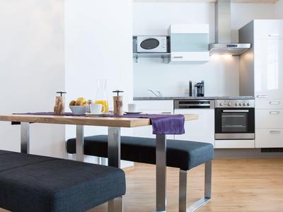 Moderne helle Küchenzeile mit Holztisch und gepolsterten Sitzbänken in einem Hotelzimmer.