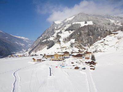 Schneebedecktes Tal mit Chalet-Dorf und Nebel über den Bergen bei klarem Himmel