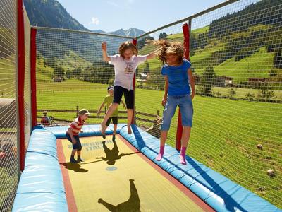 Kinder springen auf einem Trampolin im Freien vor Berglandschaft
