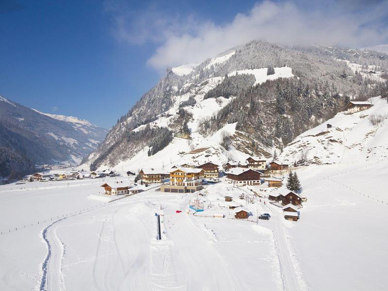Schneebedecktes Tal mit Chalet-Dorf und Nebel über den Bergen bei klarem Himmel
