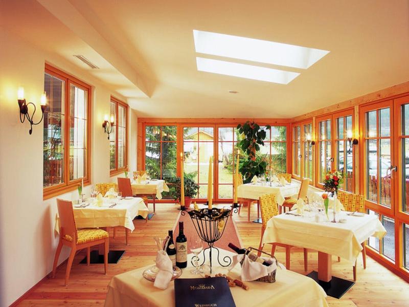 Heller Wintergarten mit Holzboden, großen Fenstern, gedeckten Tischen und gemütlicher Atmosphäre.