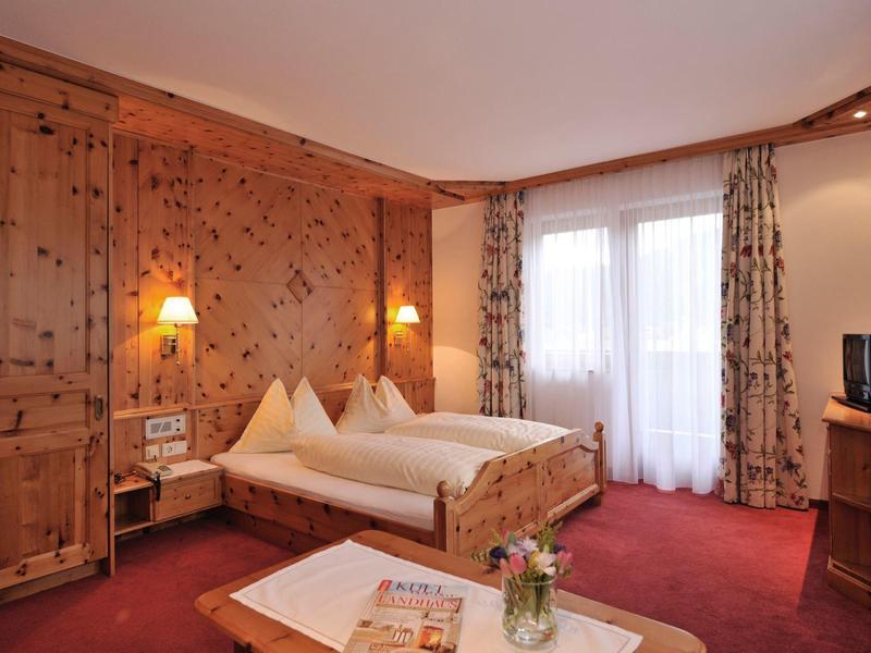 Gemütliches Schlafzimmer mit Holzmöbeln, roten Teppichen, zwei Betten und Balkon vor Vorhängen.