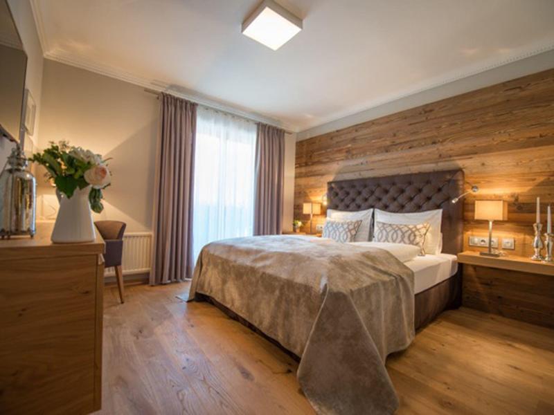 Gemütliches Schlafzimmer mit Holzwand, großem Bett, Nachttischen und Vorhängen am Fenster.