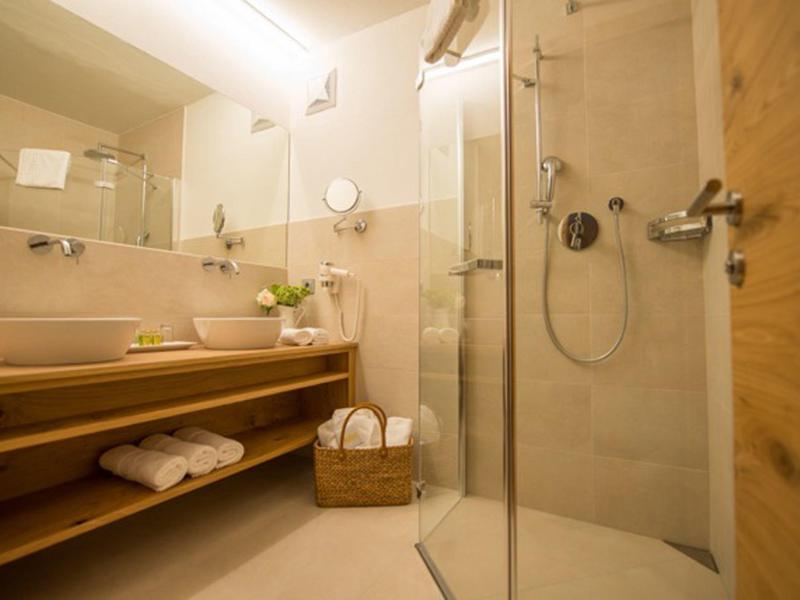 Modernes Badezimmer mit großer Spiegelwand, Glasdusche, Holzregal und hellen Fliesen.