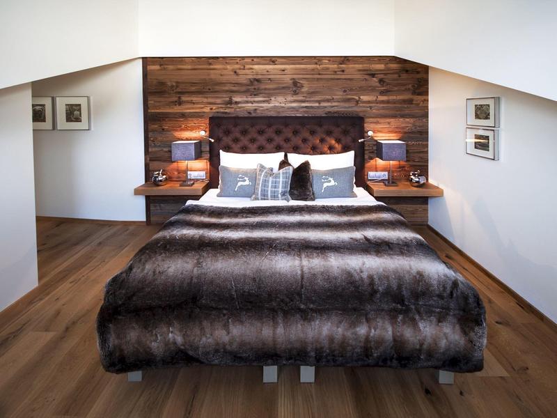 Gemütliches Schlafzimmer mit braunem Holzboden, dunklem Bett und rustikaler Holz-Wandverkleidung.