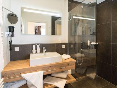 Salle de bains moderne avec meuble en bois et douche en verre aux tons chauds.