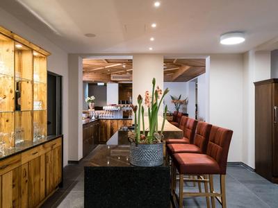 Moderner Sitzbereich mit rotem Polster, zentralem Tisch und beleuchtetem Vitrinenschrank aus Holz.