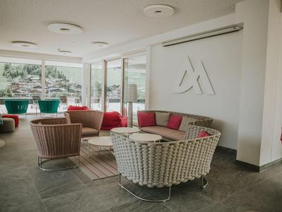 Salon lumineux avec fauteuils et canapés en osier modernes, grandes fenêtres et vue sur la montagne.