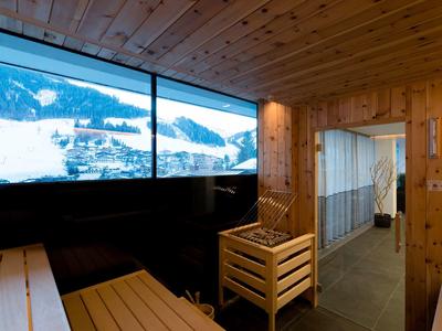 Sauna en bois avec fenêtre panoramique donnant sur des montagnes enneigées en hiver.