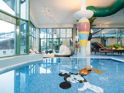 Piscine intérieure avec colonne colorée et espace enfants dans un hôtel avec fenêtres panoramiques.