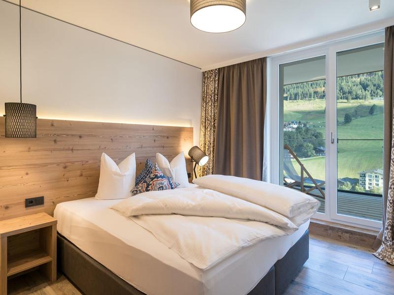 Chambre moderne avec grand lit, mur d'accent en bois et accès au balcon avec vue sur paysage verdoyant.