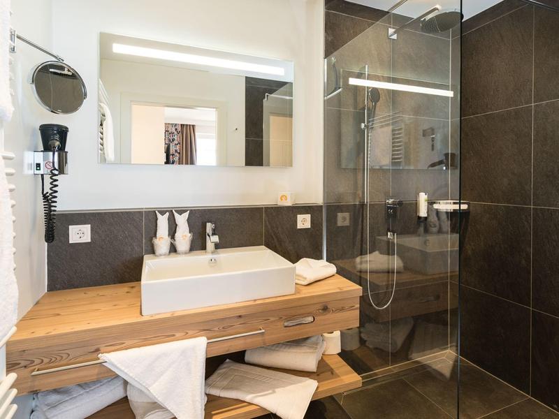 Salle de bains moderne avec lavabo en bois, grand miroir et douche à l'italienne avec carrelage foncé.
