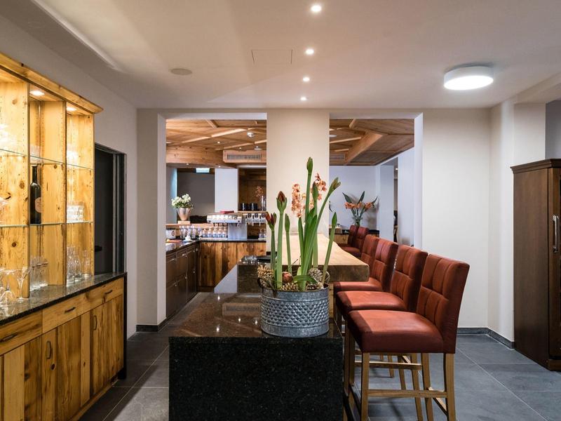 Espace bar moderne d'hôtel avec tabourets rouges et vitrine en bois éclairée.
