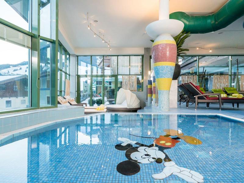 Piscine intérieure avec colonne colorée et espace enfants dans un hôtel avec fenêtres panoramiques.