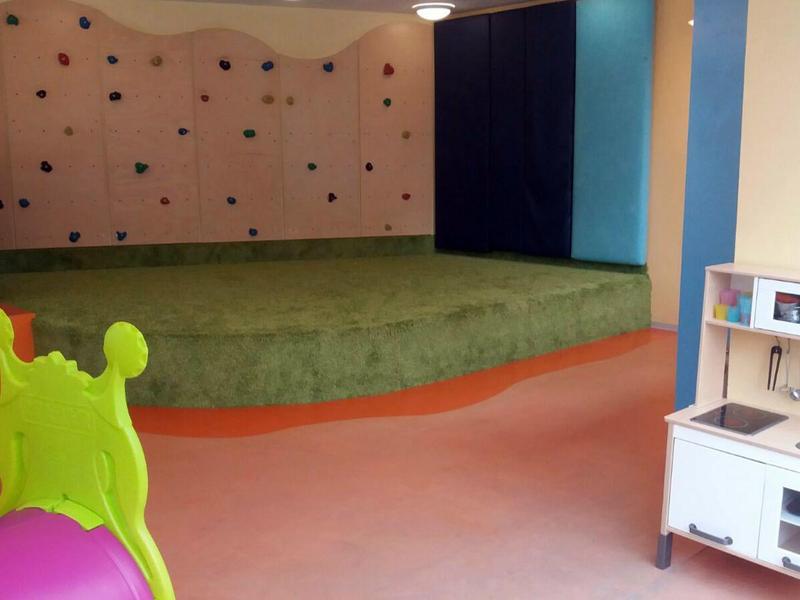 Un espace de jeu coloré avec une structure d'escalade verte et une scène douce dans un hôtel.