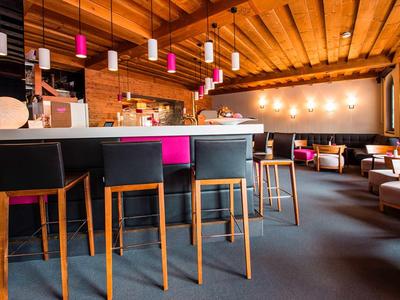 Modern eingerichtete Bar mit Holzdecke, farbigen Barhockern und gemütlichen Sitzbereichen.