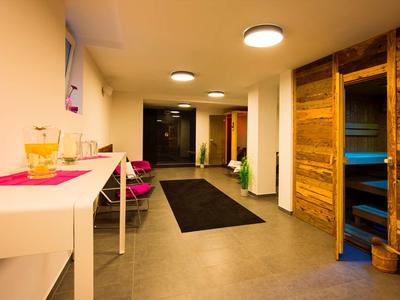 Heller Flur mit Holzsauna, weißen Wänden, grauem Boden und mehreren Deckenlampen.