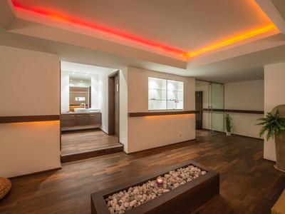 Moderner Raum mit dunklem Holzboden, weißen Wänden, indirekter bunter Deckenbeleuchtung und Pflanzen.